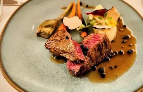 Assiette avec deux morceaux de steak rosé accompagnés de sauce, carottes, champignons et garniture décorative sur une table dressée.
